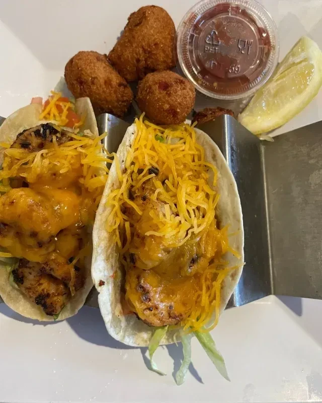 Two tacos in a holder, with fried balls, sauce, and lemon.