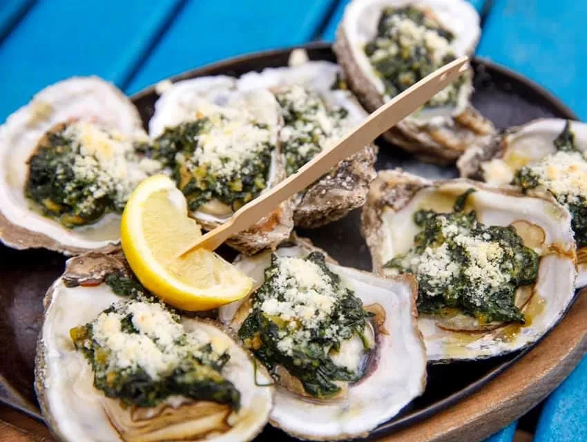 Baked oysters in shells, topped with green herbs and cheese, with lemon.