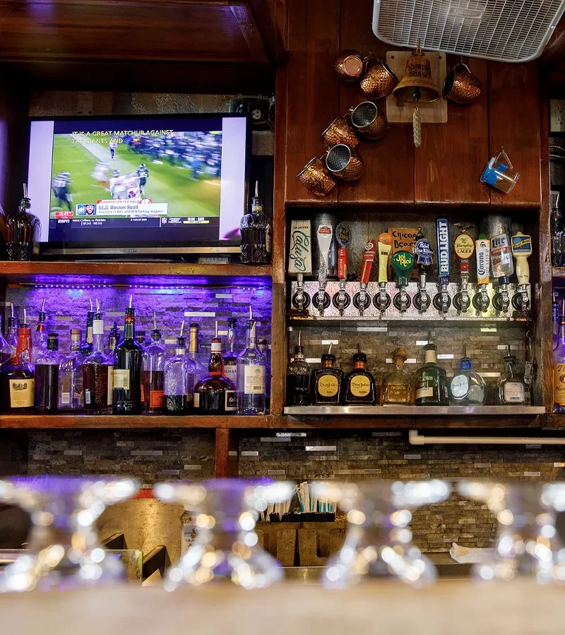 Bar with liquor bottles, beer taps, purple LEDs, and sports on TV.