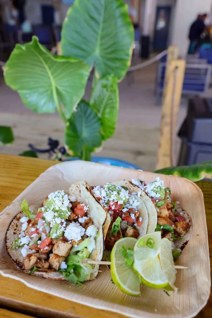 Three chicken tacos with guacamole, lime, on a natural plate outdoors.