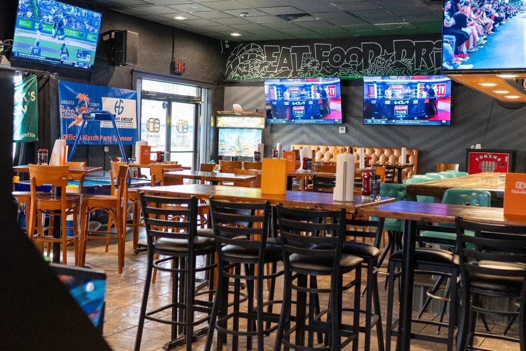 Casual sports bar interior with wooden tables, dark walls, and multiple sports TVs.