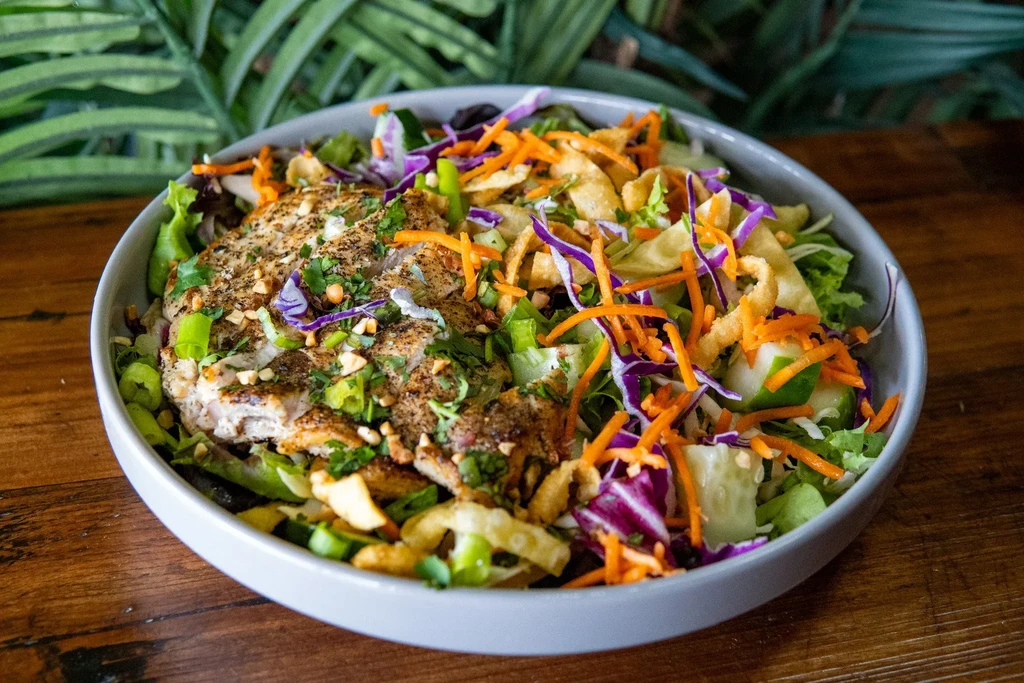Vibrant grilled chicken salad in a bowl on a rustic wooden table.