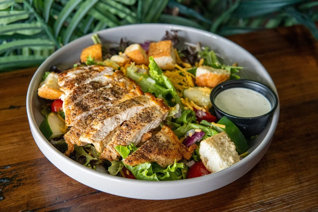 Close-up grilled chicken salad with greens, tomatoes, cheese, and dressing.