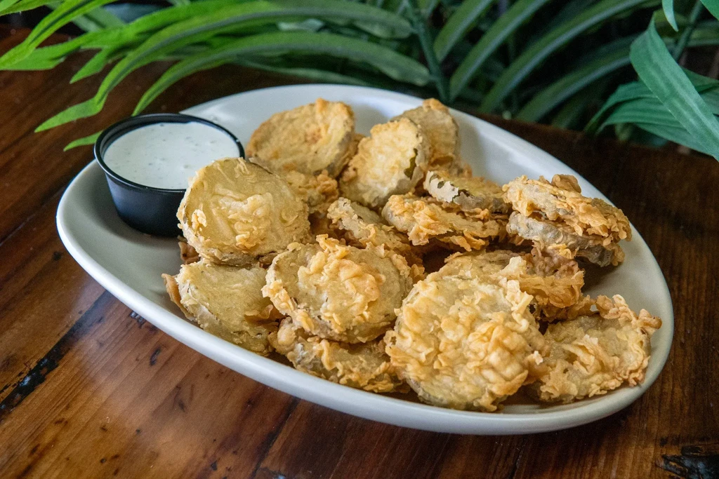 Crispy fried pickles with dipping sauce on a rustic wooden table.