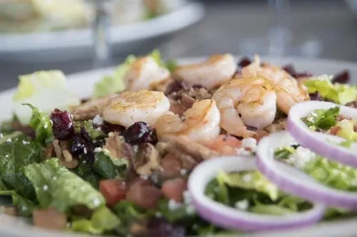 Colorful shrimp salad with mixed greens, cranberries, feta, and red onion.
