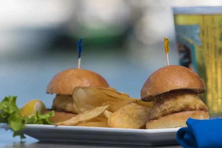 Two sliders, potato chips, lettuce, and lemon on a white plate.