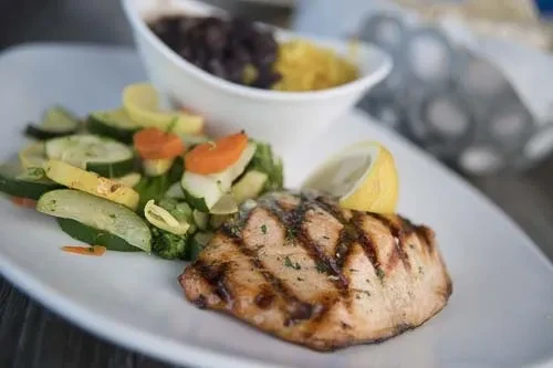 Grilled fish fillet, colorful vegetables, yellow rice, and black beans.