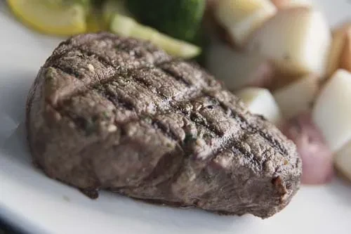 Close-up of grilled steak with grill marks, lemon, and roasted potatoes.