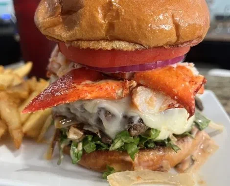 Stacked beef and lobster burger with melted cheese and fries.