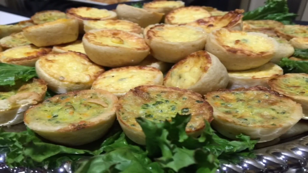 Platter of golden mini quiches with herb filling and lettuce garnish.
