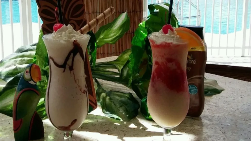 Tropical frozen drinks with whipped cream, cherries, and a parrot figurine.