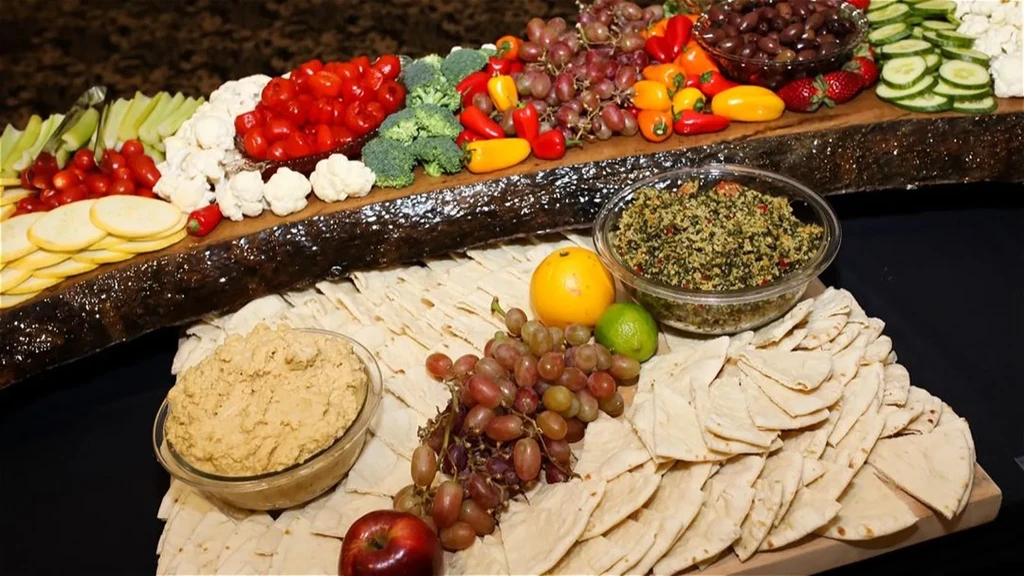 Vibrant fresh vegetables, fruits, dips, and flatbreads on a wooden board.