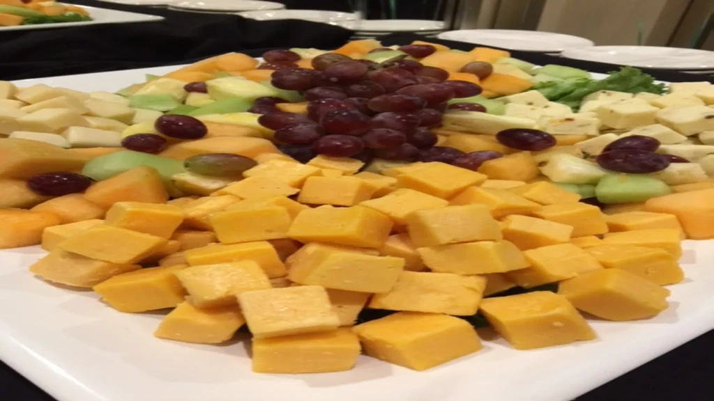 White platter with orange cheddar, mixed cheese cubes, melon, and grapes.