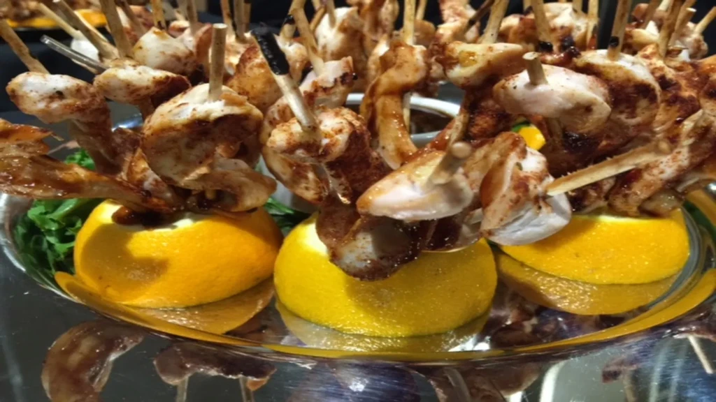 Seasoned meat skewers with citrus and greens on a silver platter.