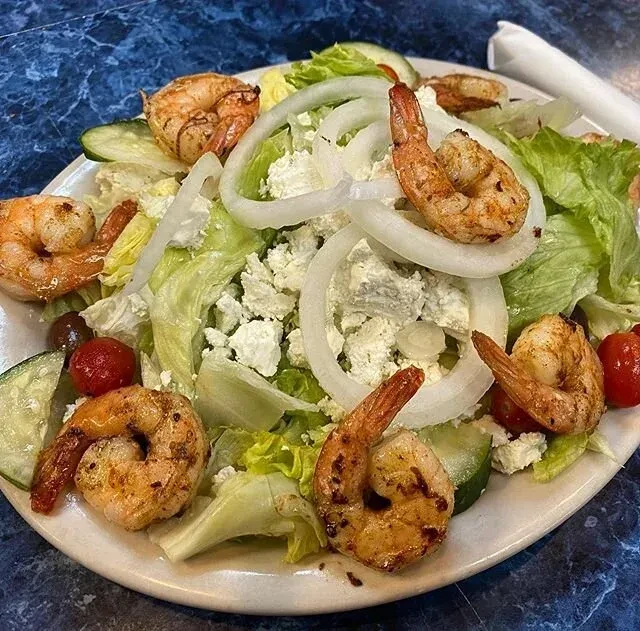 Close-up of grilled shrimp salad with lettuce, feta, tomatoes, and olives.