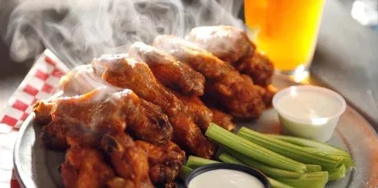 Steaming golden chicken wings, celery sticks, and two dipping sauces.