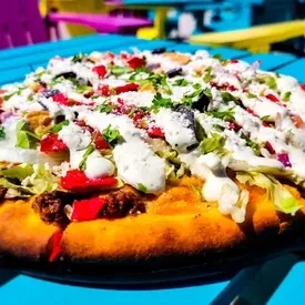 Close-up of a colorful taco pizza with creamy sauce on a turquoise table.