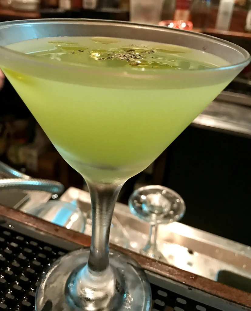 Cold light green cocktail in martini glass, with oil droplets and spices.