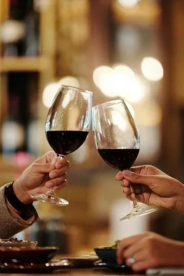 Two hands clinking red wine glasses.