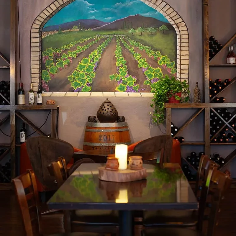 Warm wine bar with vineyard mural, candlelit table, and wine shelves.