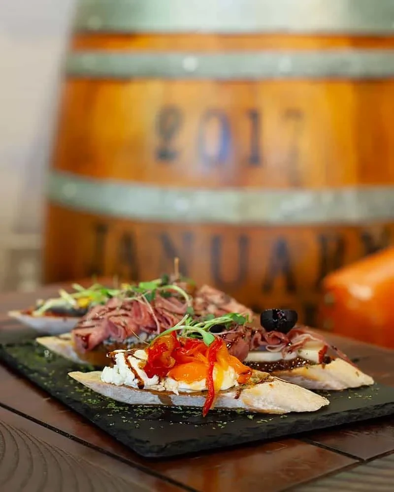 Four gourmet bruschetta or crostini on slate board, blurred barrel.