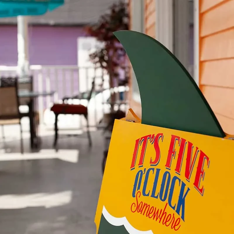 Vibrant yellow sign with green shark fin reads "IT'S FIVE O'CLOCK Somewhere".