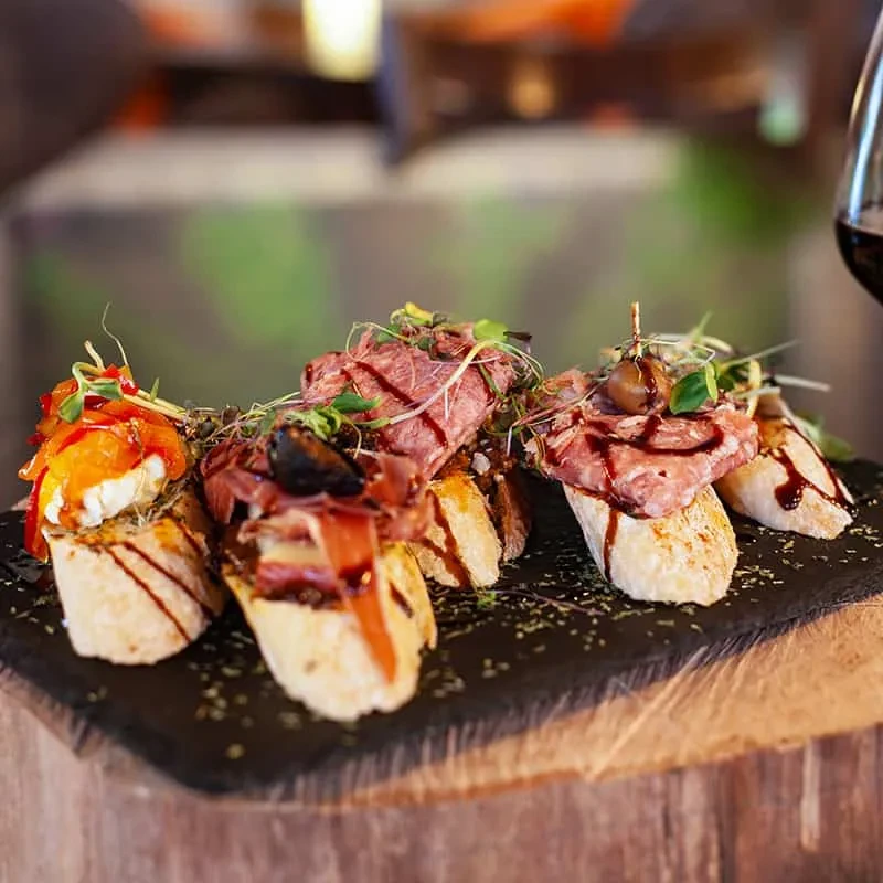 Gourmet crostini appetizers with cheese, meat, and figs on a dark board.