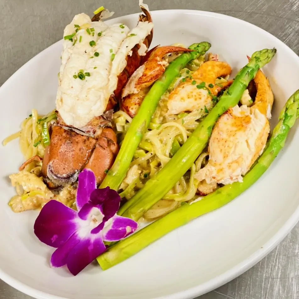 Lobster pasta with asparagus, chives, and a decorative purple orchid.