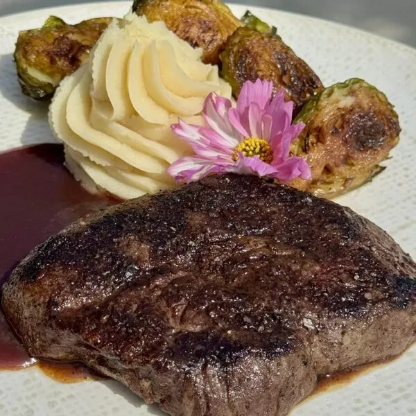 Seared steak, mashed potatoes, roasted Brussels sprouts, sauce, and flower.