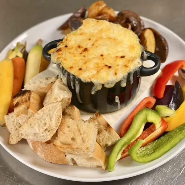 Bubbly cheese dip in pot with bread, peppers, and roasted vegetables.