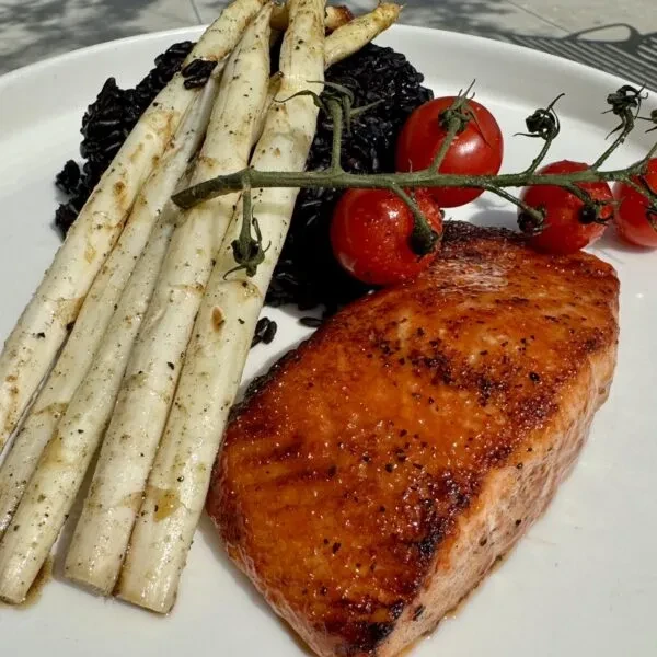 Plated seared salmon, white asparagus, dark rice, and vine tomatoes.