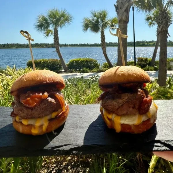 Two gourmet burgers on a dark board overlooking tropical water.