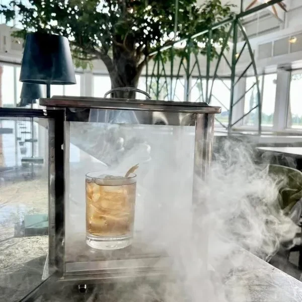 Amber cocktail in smoking chamber, white smoke billows out.
