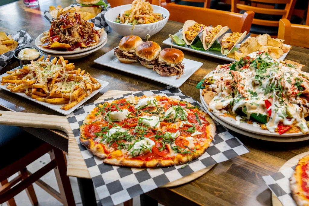 Restaurant table with pizza, nachos, tacos, sliders, and cheesy fries.