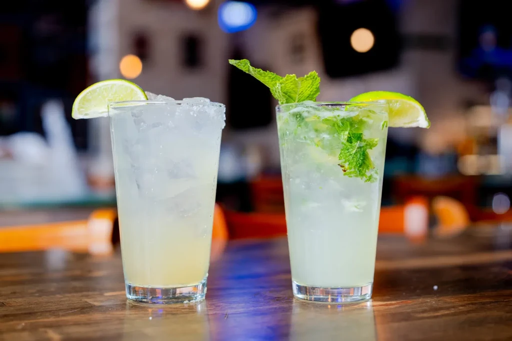 Two iced cocktails: one salted lime, one mint mojito, on a bar.