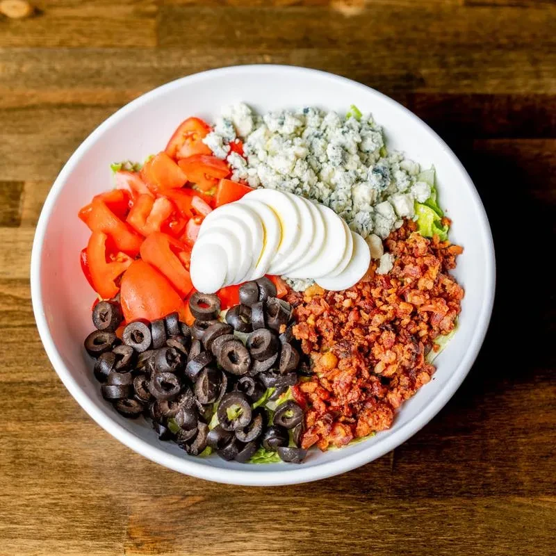 Colorful salad in white bowl with blue cheese, bacon, egg, tomato.