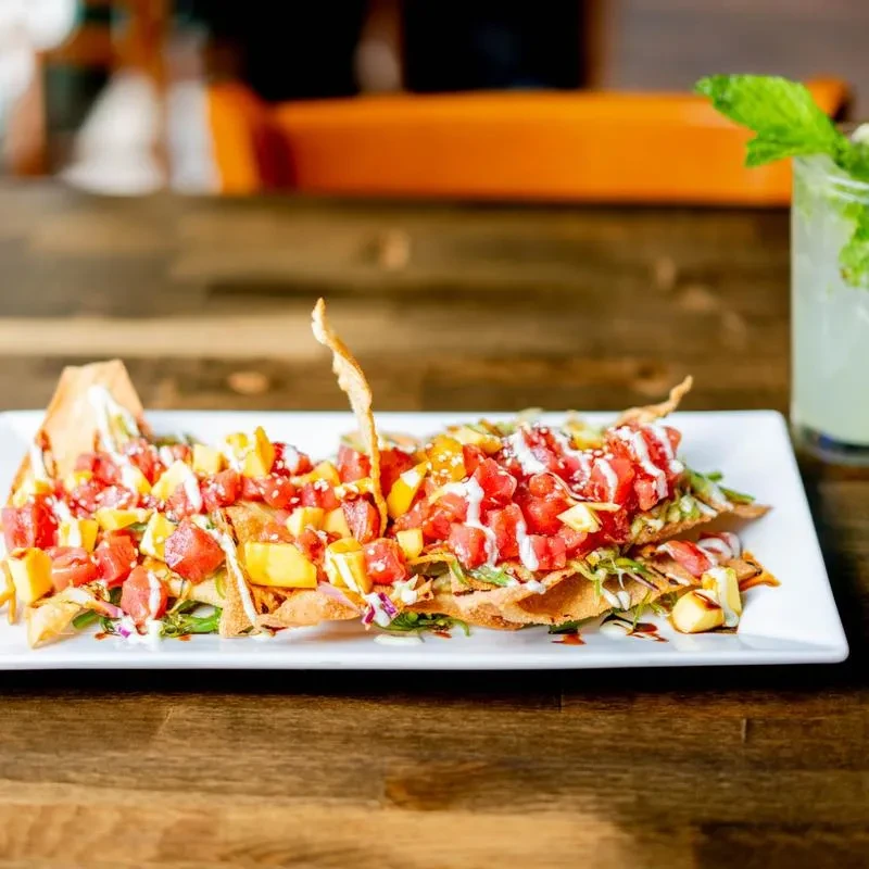 Tuna poke nachos with mango, sesame seeds, and drizzled sauces.
