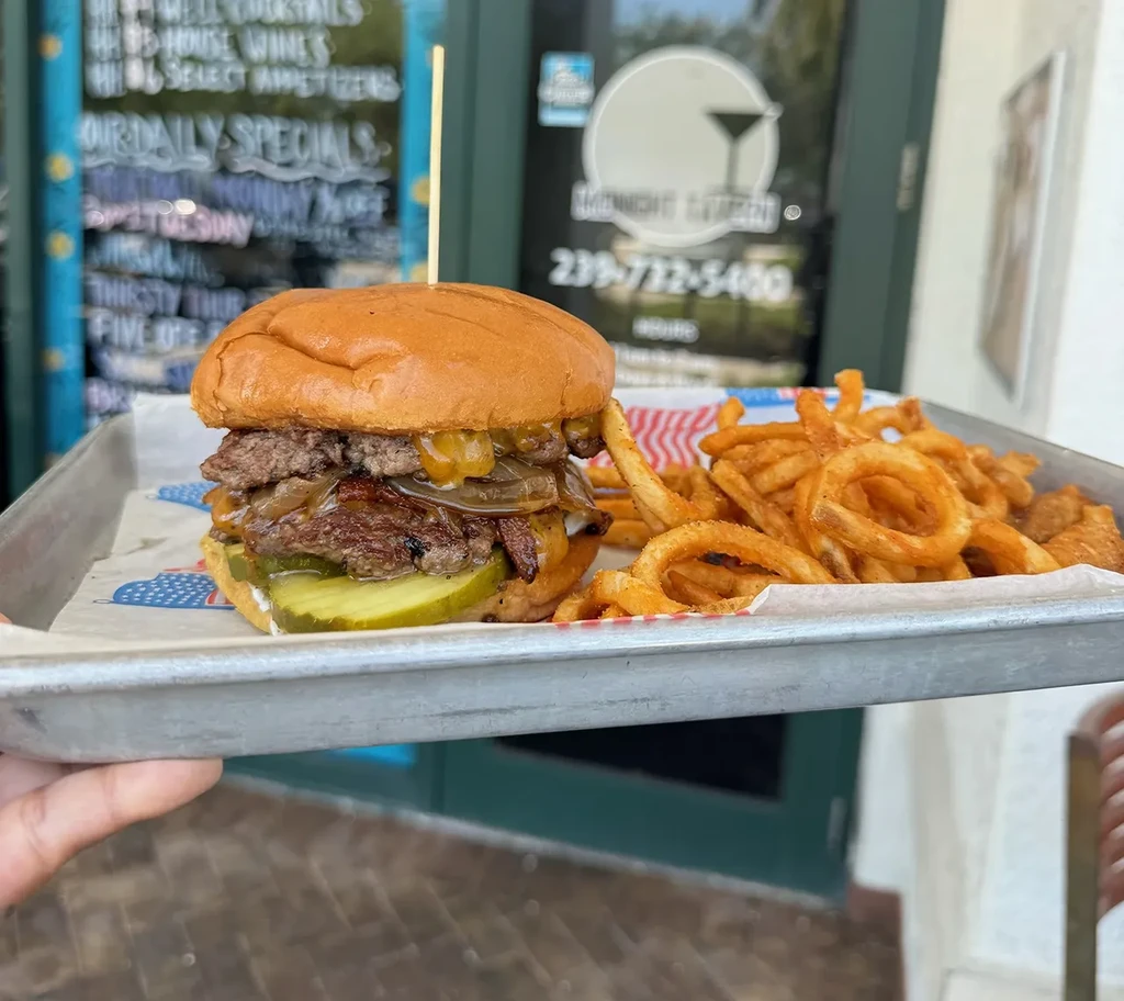 Double-patty burger with curly fries on a metal tray.