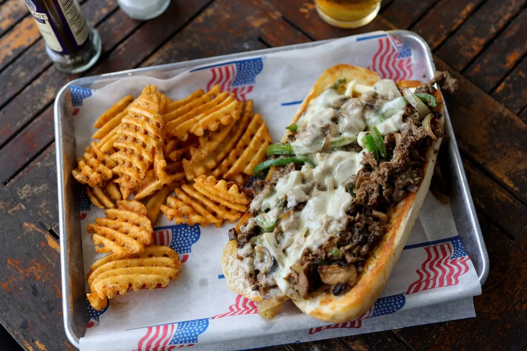 Cheesesteak-style sandwich and waffle fries on flag-patterned tray.