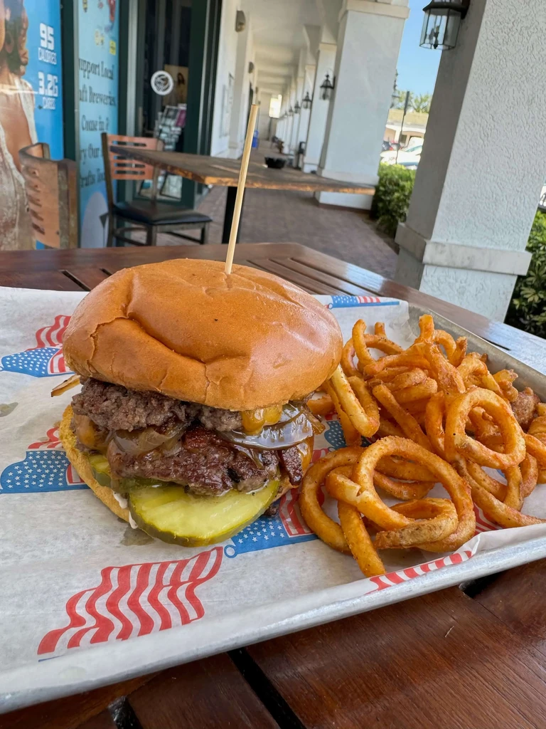A double burger and curly fries served on an an outdoor tray.