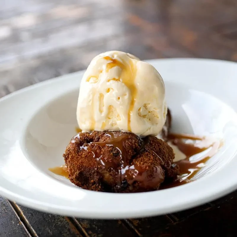 Warm dark brown dessert topped with caramel and melting vanilla ice cream.