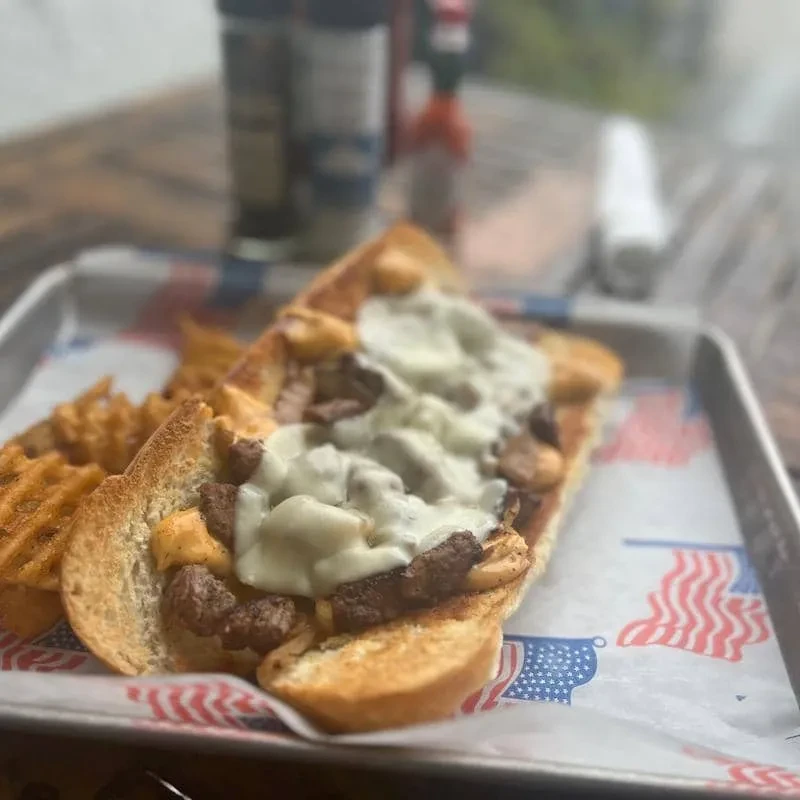Cheesesteak-style sandwich with meat, onions, cheese sauce, and waffle fries.