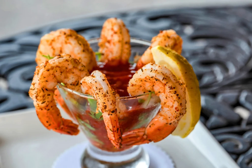 Plump, seasoned shrimp cocktail with red sauce and lemon wedge.