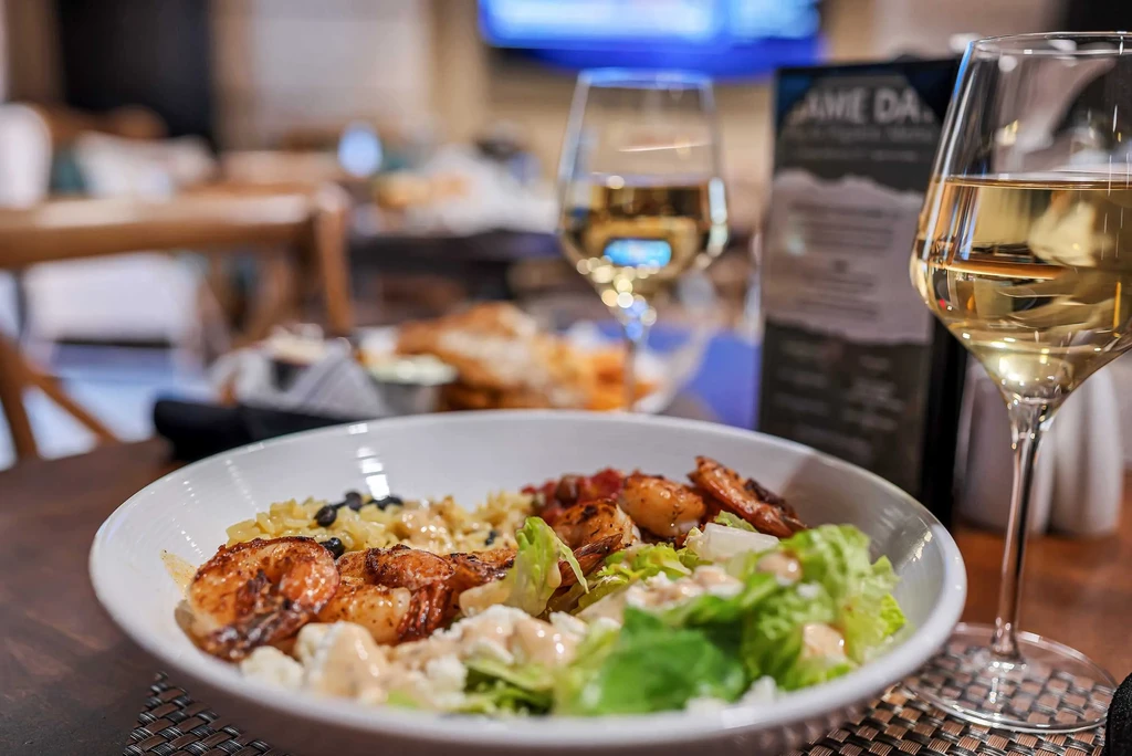 Close-up of shrimp grain bowl and white wine on wooden table.