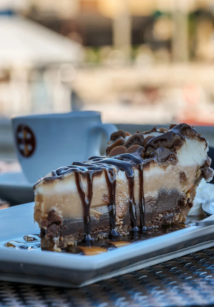 Multi-layered dessert slice with chocolate, caramel, cream, and chocolate sauce.