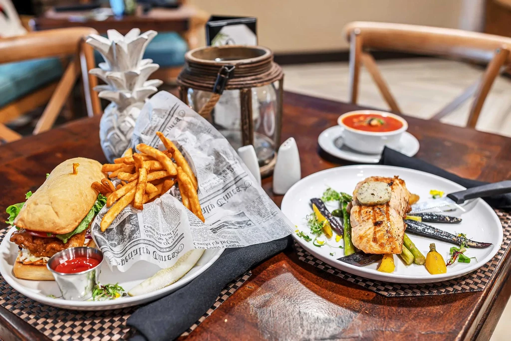 Large sandwich with fries and grilled salmon with roasted vegetables.