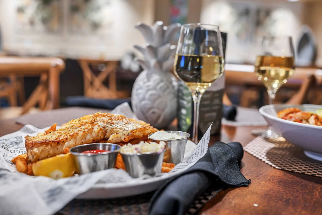Fish and chips with sauces and white wine on a restaurant table.