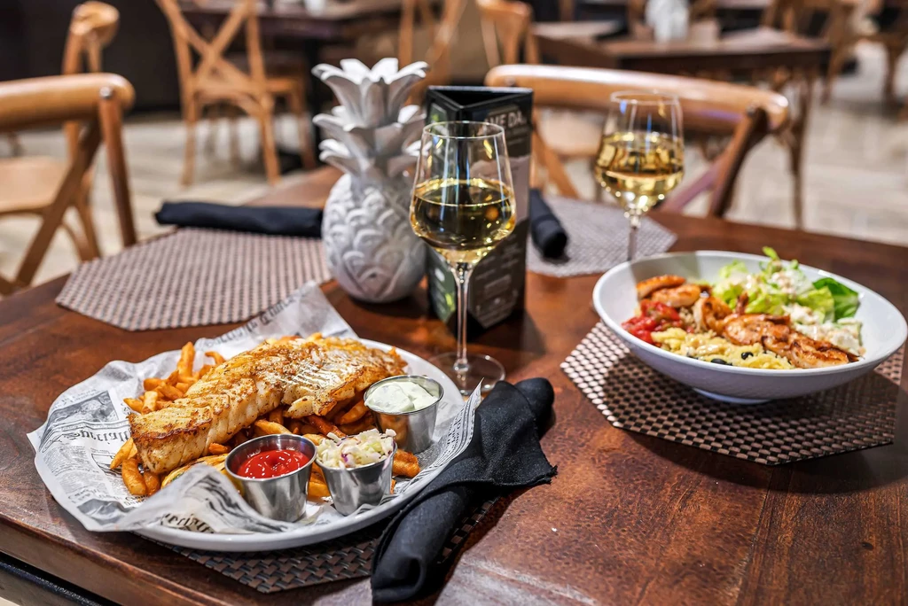 Restaurant dining table with fish and chips, shrimp salad, and white wine.