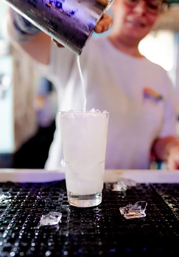 A light liquid pours from a shaker into an ice-filled glass.