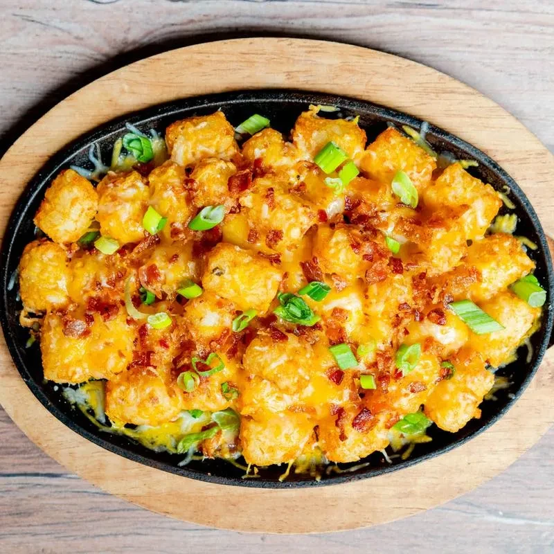Loaded tater tots in a skillet with melted cheese, bacon, and green onions.